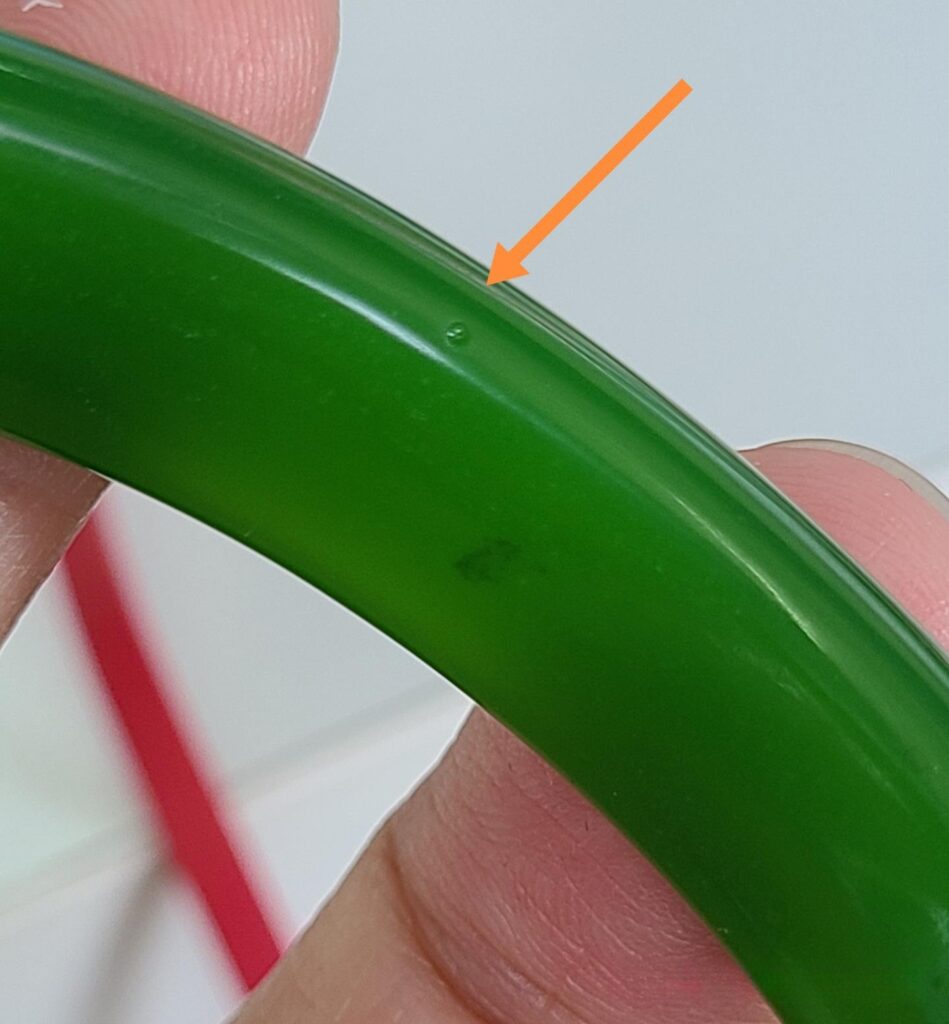 Close-up of an emulsified glass bangle surface, showing hemispherical pits—the result of polishing revealing internal bubbles