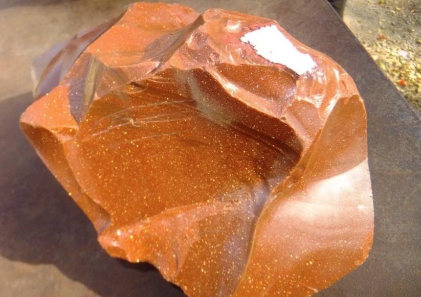 Close-up view of a broken Goldstone glass piece, clearly displaying the characteristic conchoidal (shell-like) fracture.