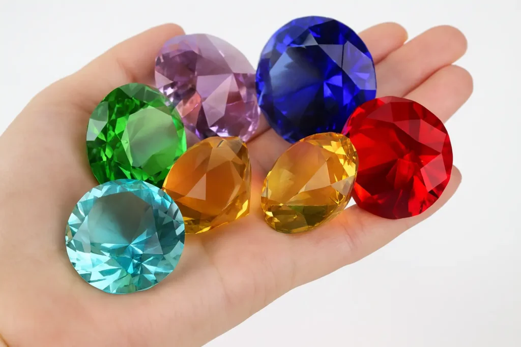 Hands holding an assortment of vibrant, brightly colored liuli (glass) imitation gemstones, showing the wide range of colors achievable