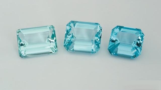 Three faceted aquamarine gemstones lined up, showing the color gradient from light bluish-green to saturated deep blue, illustrating value difference.