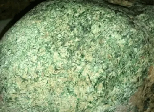 Jadeite rough stone with xian pattern — irregular black, dark green, or gray spots appearing on the weathered skin surface.