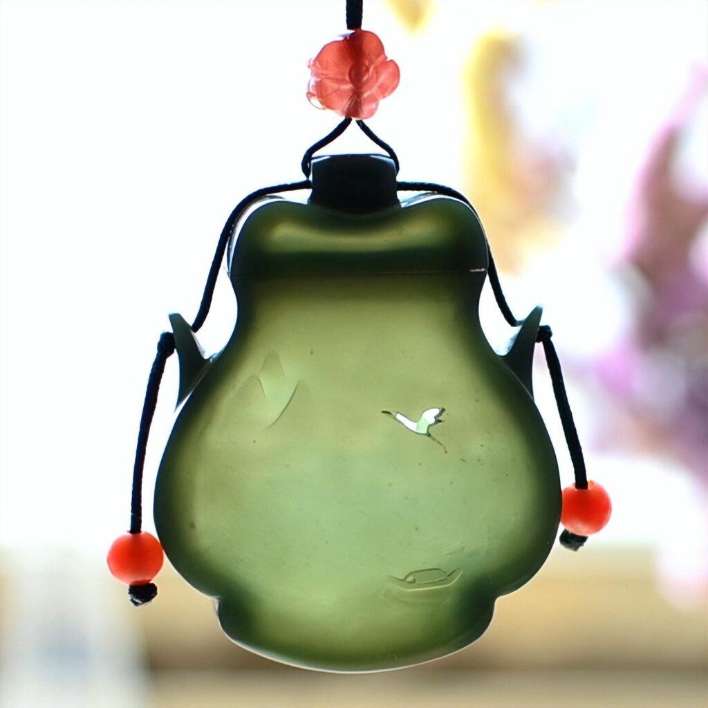 A custom-designed Hetian Celadon Jade (Qingyu) sachet carving from Jewea, showcasing the rare and delicate thin-wall (Bo Tai) carving technique, which achieves exquisite translucency.