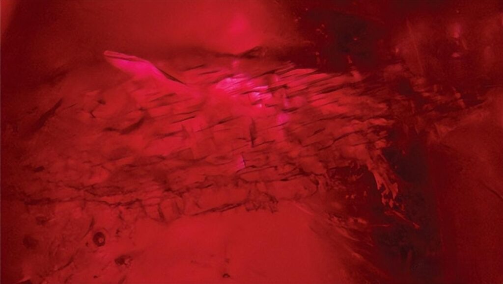 Microscopic view of a lead glass filled ruby, showing gas bubbles and visible filling material in the internal fracture.