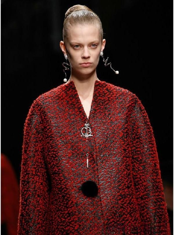 Model wearing a brooch at the center of a coat’s chest, showcasing a clean, strong, and subtly sensual style.