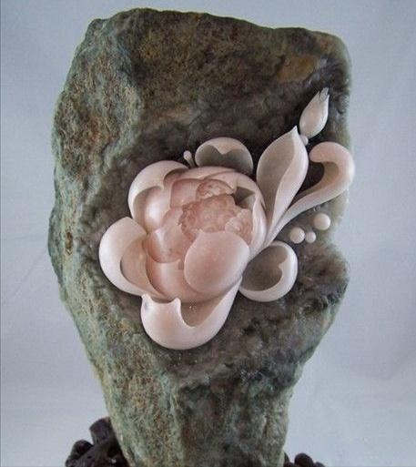 A flower carved from a stone, utilizing the subtle pale pink and lavender hues of the purple jade for a stunning effect.