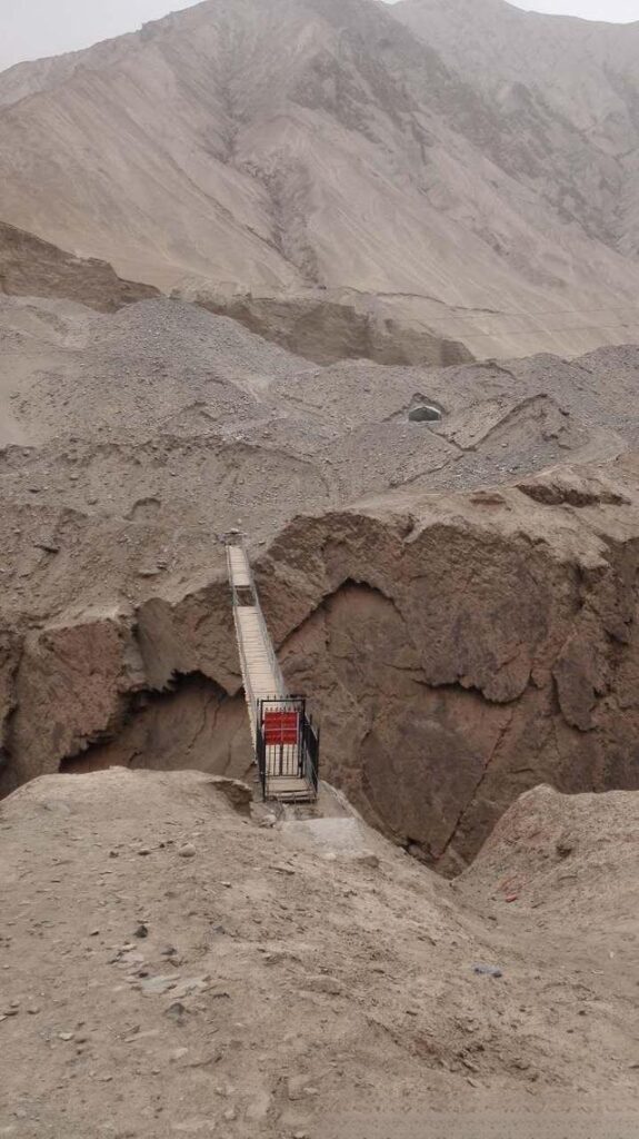 Miners crossing a primitive bridge on a sheer cliff in the Kunlun Mountains.