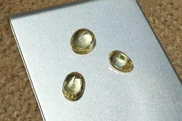 Three gemstones that have lost nearly all saturation, appearing almost colorless with only a trace of yellow.