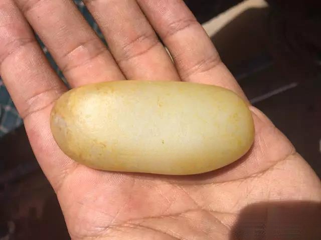Close-up of a hand holding a Ziyu (seed jade) stone from the Qushou river section, displaying a thin layer of light gold sprinkle skin.