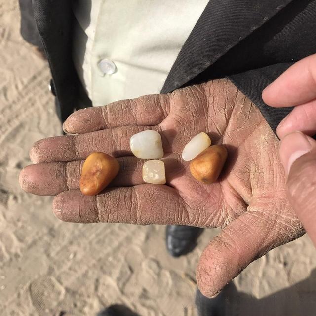 A miner’s weathered palm holding small, smooth Hetian seed jade pebbles.
