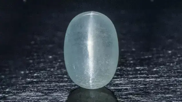 A rare oval white Zircon gemstone displaying a distinct band of reflected light, known as the cat's eye effect.