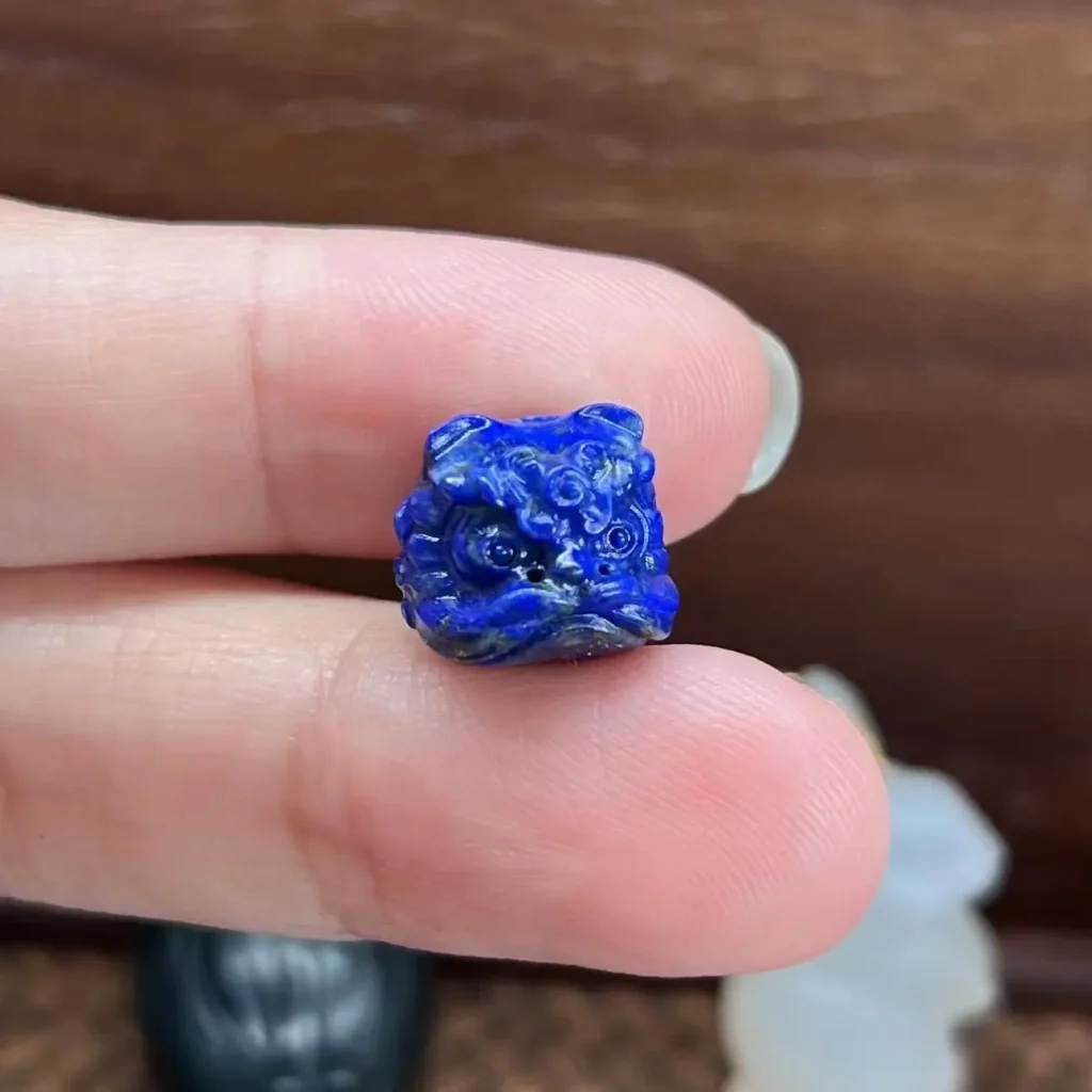 A hand holding a Guochao-style dancing lion statue crafted from natural Afghanistan Lapis Lazuli.