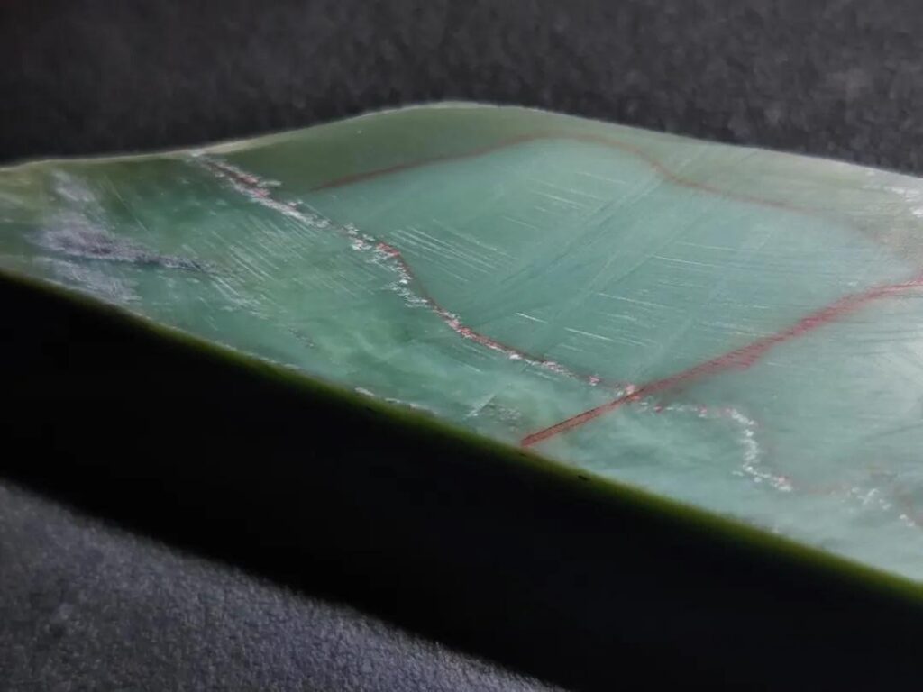 Faceted Afghan nephrite section showing a coarse internal structure, dark hue, and black inclusions.