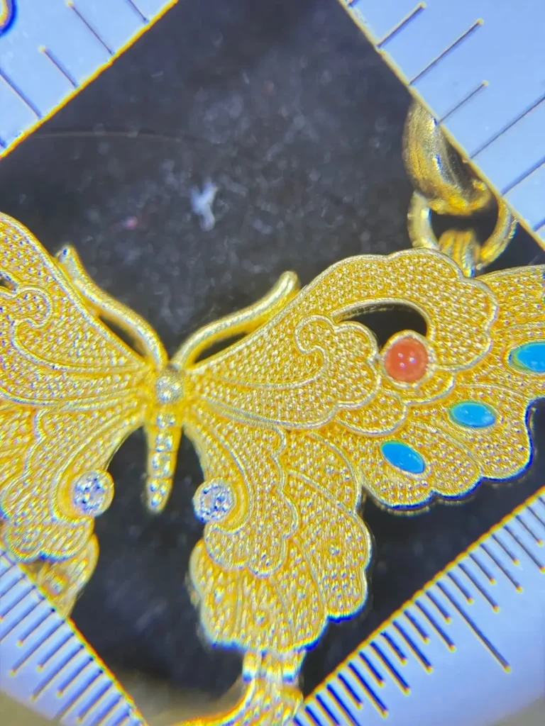 Close-up of a gold butterfly granulation jewelry piece featuring hundreds of hand-placed microscopic gold beads.