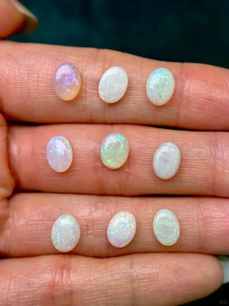 Nine small white opals in a palm showing sweet candy-like pastel play-of-color and neon flashes.