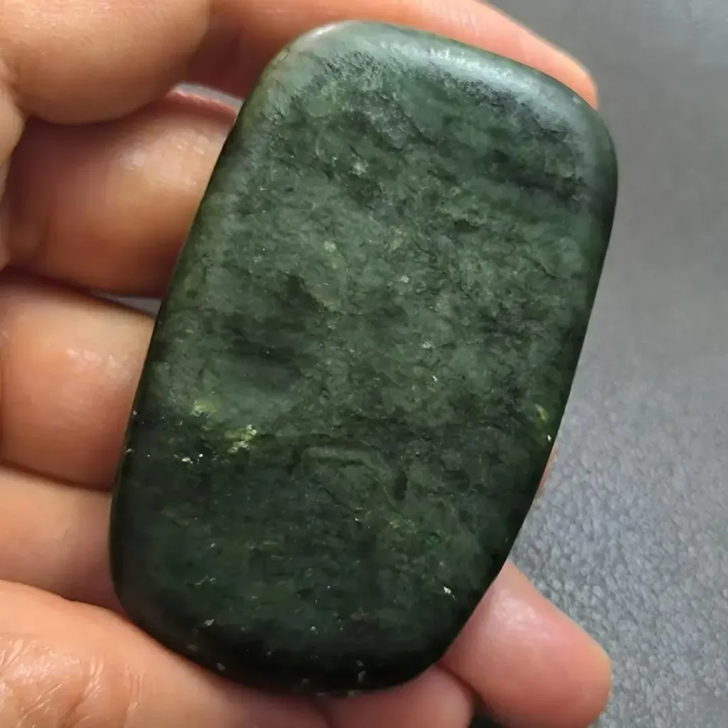 A river-worn New Zealand Pounamu nephrite stone with bright green translucency and black inclusions.
