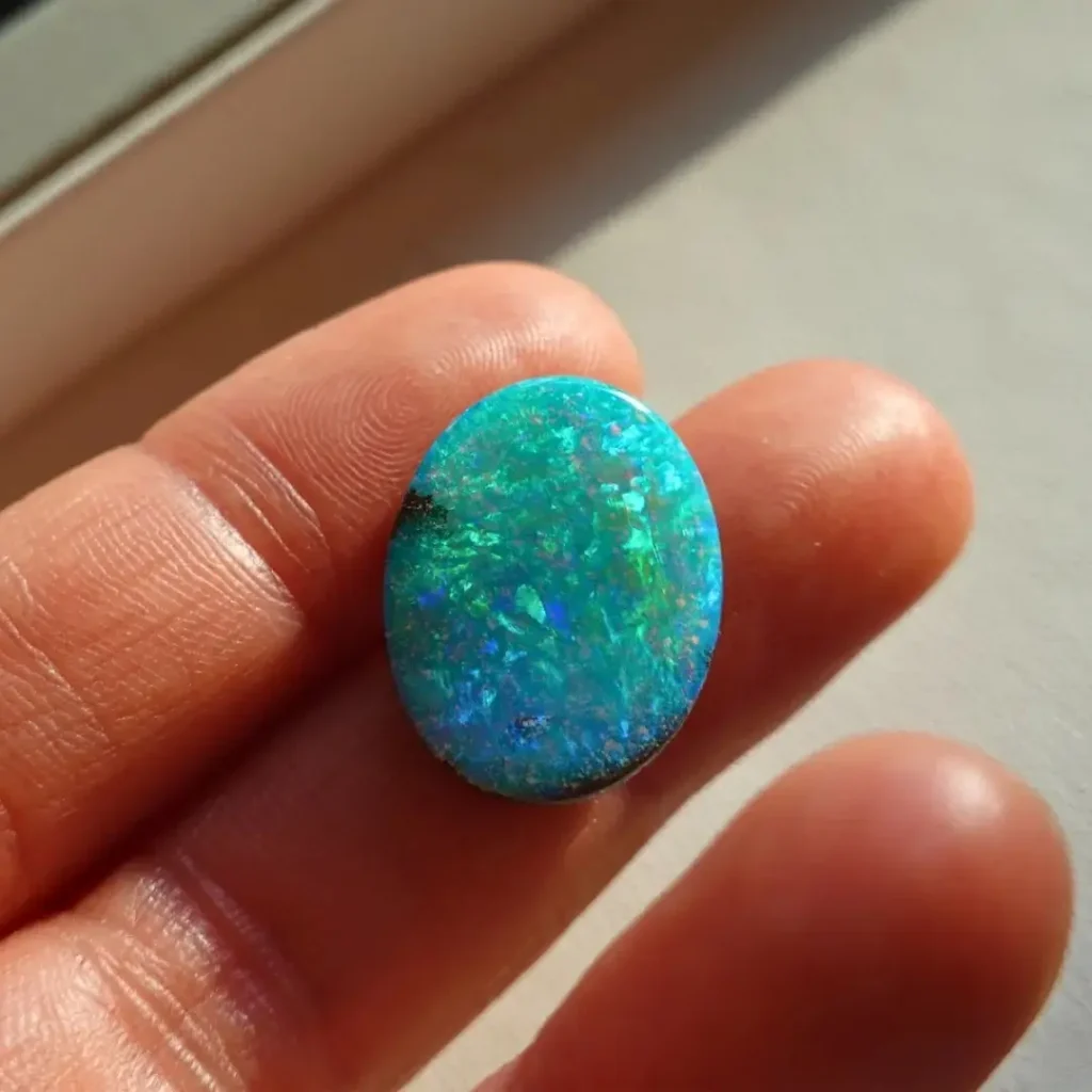 Shanyu holding a refined Queensland Boulder Opal with vibrant spectral colors against a dark ironstone matrix.