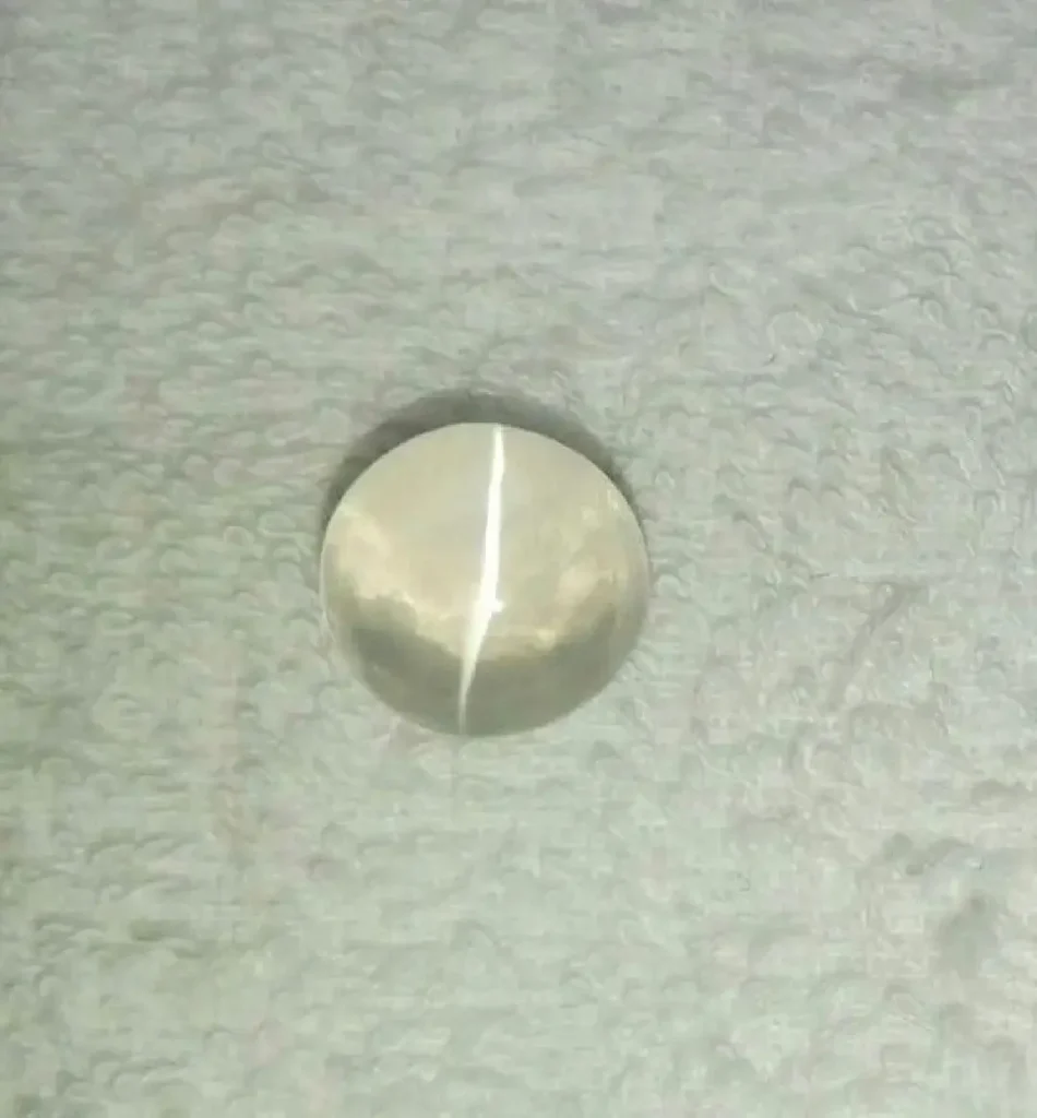 White quartz cabochon displaying a single sharp cat’s eye light band caused by chatoyancy.