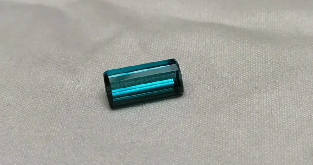A deep Indigo blue tourmaline gemstone resting on a textured grey velvet background.
