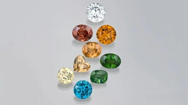 A collection of natural zircons in various colors, including blue, champagne, and warm honey tones.