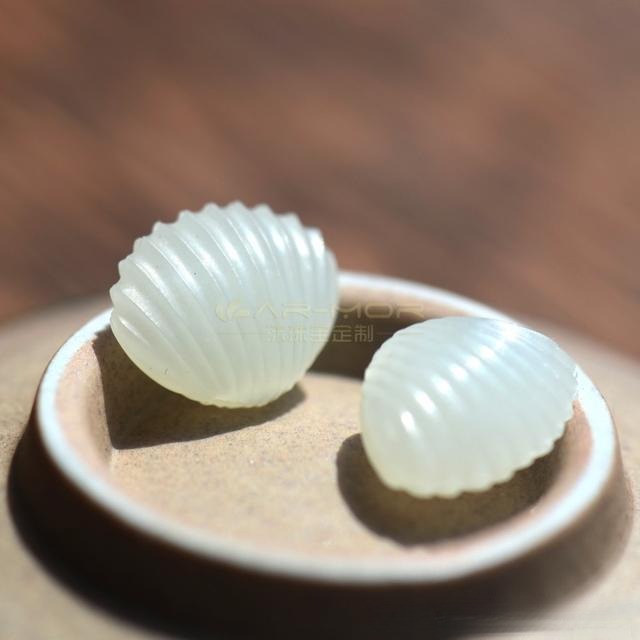 A pair of shell-carved Grade 1 White Hetian Nephrite seed jade ornaments.