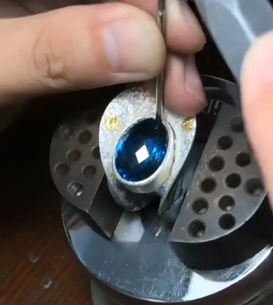 A halo ring design featuring an Ottu sapphire surrounded by diamonds in a gold setting.