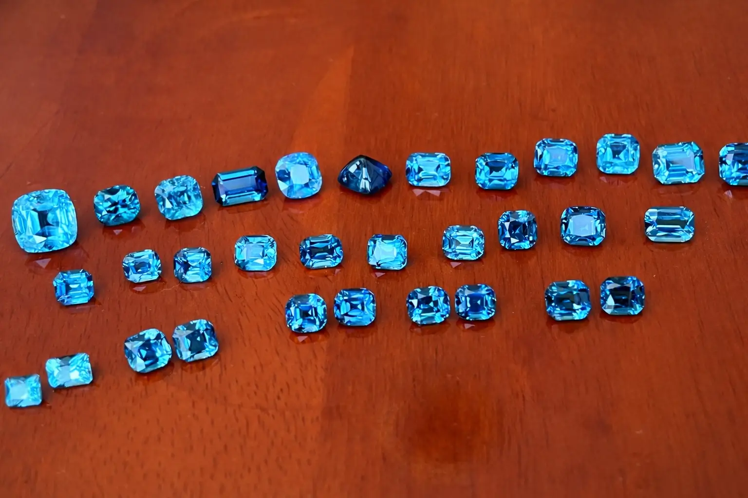 A collection of high-saturation Indigo and Lagoon tourmalines arranged on an orange-red surface.