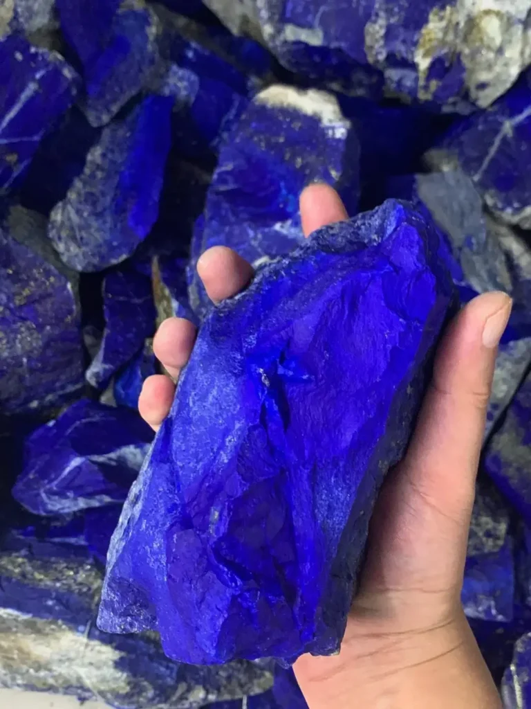 A single hand holding a raw Afghan lapis lazuli stone with deep blue lazurite and golden pyrite.