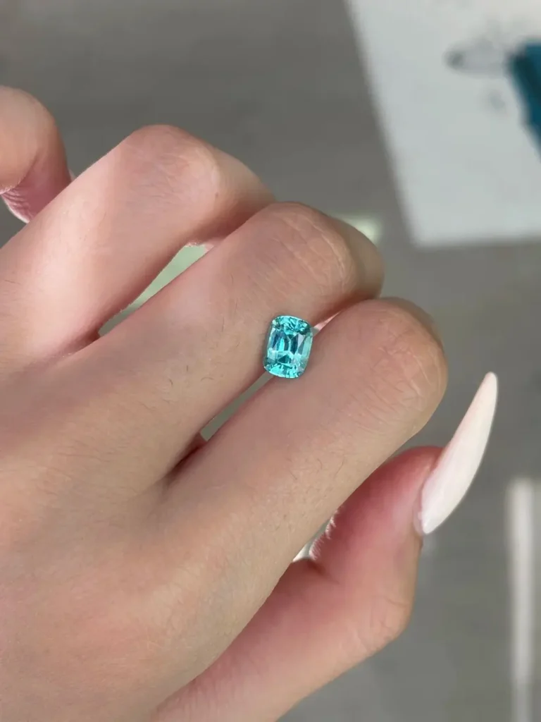 A small, vibrant Lagoon blue-green tourmaline gemstone displayed on a hand for scale and brilliance.