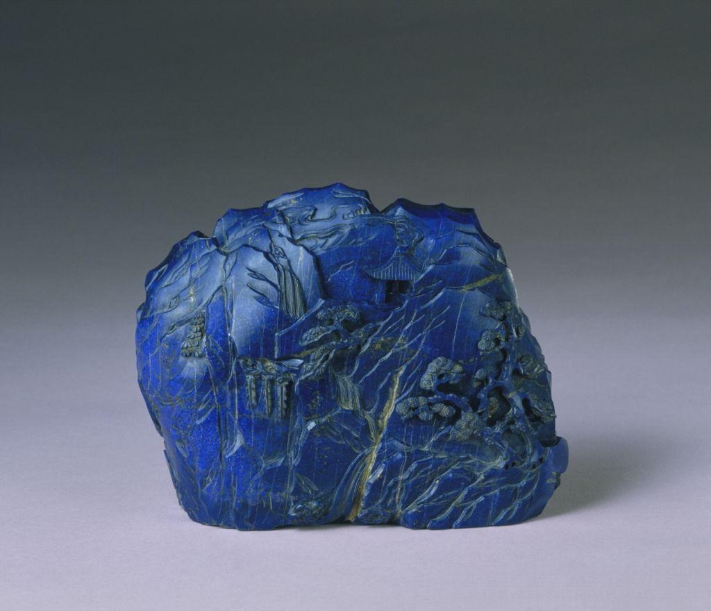 A detailed landscape carving on intense royal blue stone with uniform color saturation.