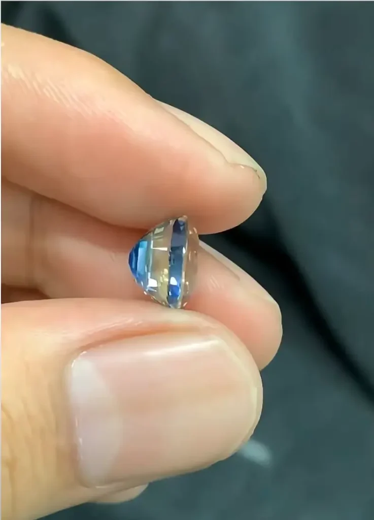 Side view of a blue gemstone showing light rays reflecting from the blue culet through the facets.