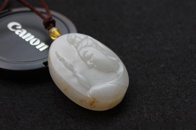 A seed jade Guanyin plaque with visible, coarse grain and uneven internal texture.