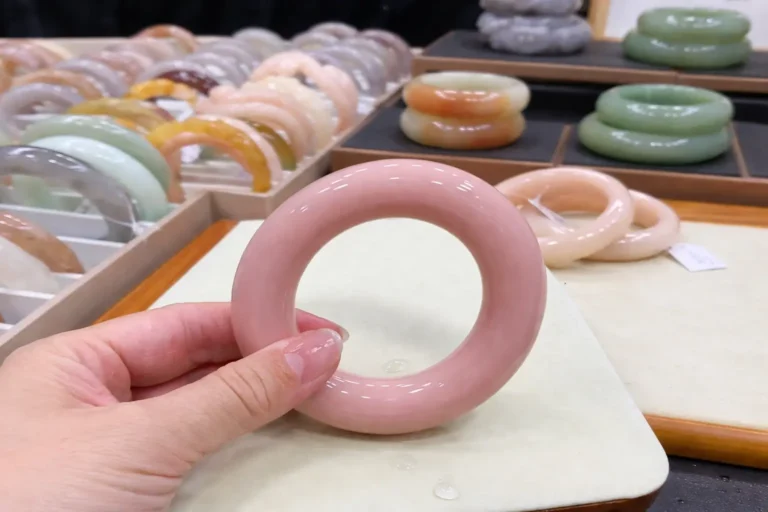 Hand holding a pink Shetaicui quartzite bracelet with colorful bracelets in the blurred background.