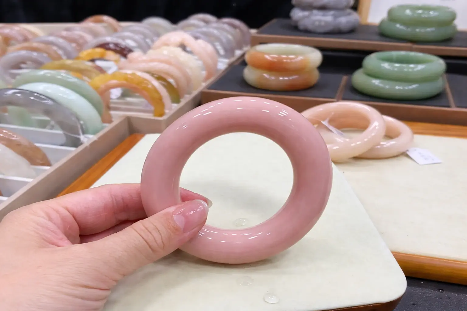 Hand holding a pink Shetaicui quartzite bracelet with colorful bracelets in the blurred background.