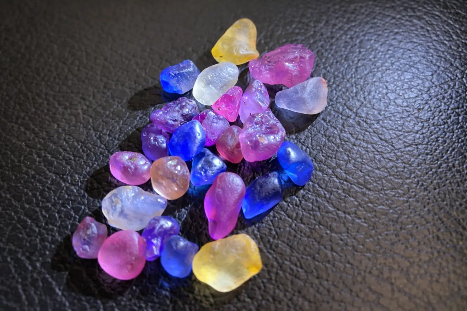 A collection of colorful Sri Lankan sapphires arranged on a textured leather gem mat.