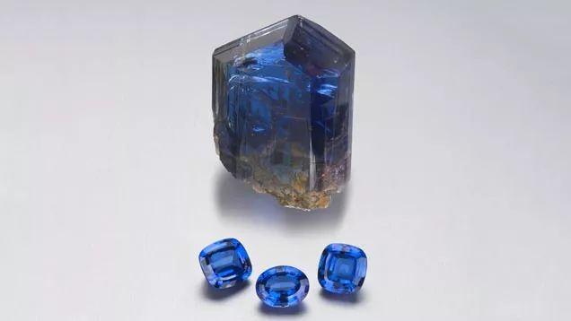 One raw Tanzanite crystal specimen alongside three faceted Tanzanite gemstones.