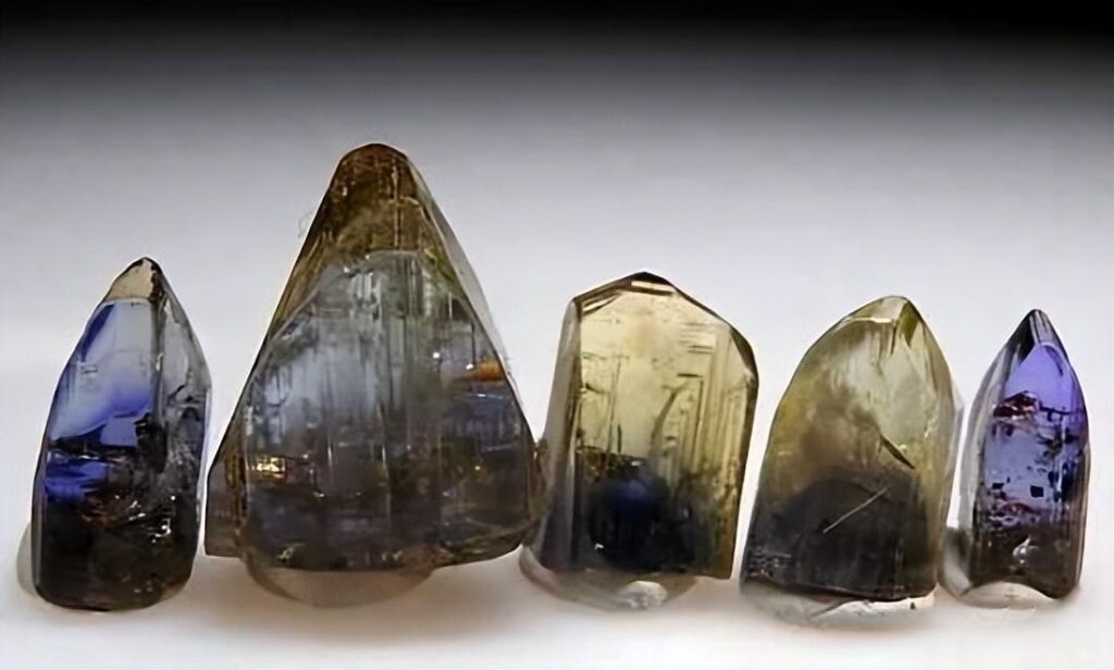 A group of raw tanzanite crystals showing red-violet, deep blue, and yellowish-green hues.
