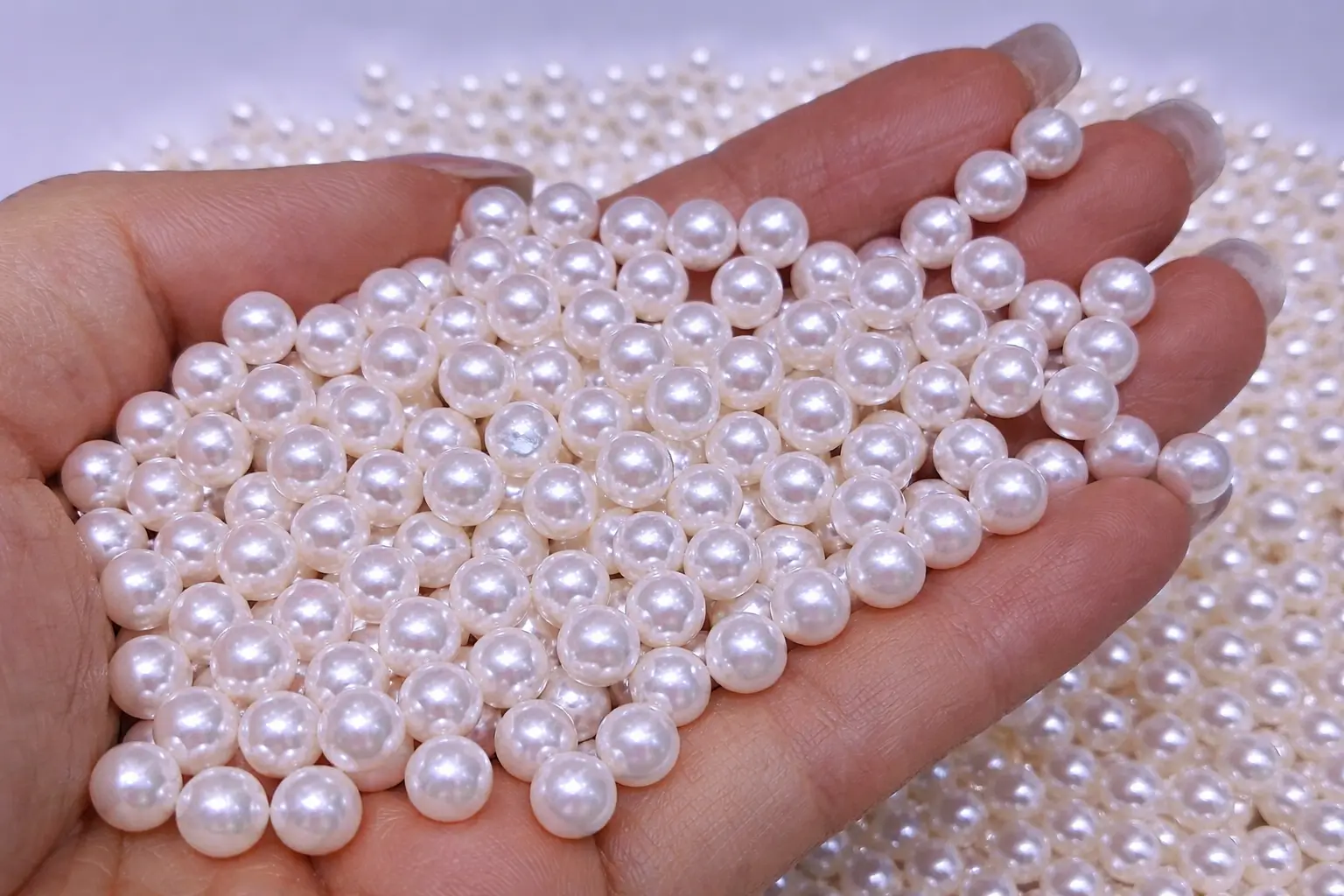 Hand-held 5.5-6mm Akoya loose pearls showing round shape, high luster, and smooth surface.