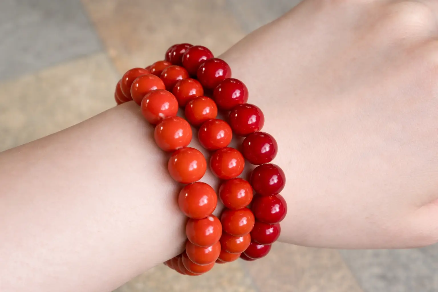 A wrist stacked with three vibrant red coral bead bracelets: Aka, Momo, and Sardinia.