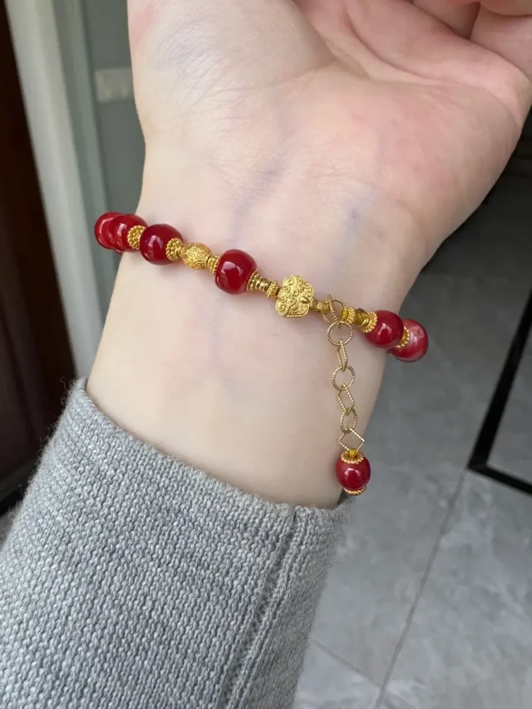 A close-up of a translucent, vibrant Aka red coral bracelet set with 18k gold on a person's wrist.
