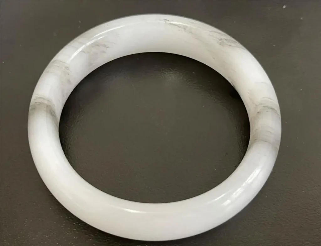 Anhydrite bangle with chalky white areas and faint, stringy black inclusions.