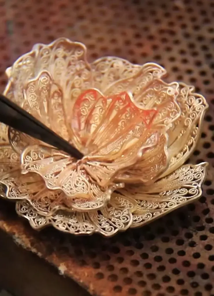 An artisan arranging small Filigree & Inlay components into a complex 3D floral jewelry piece.
