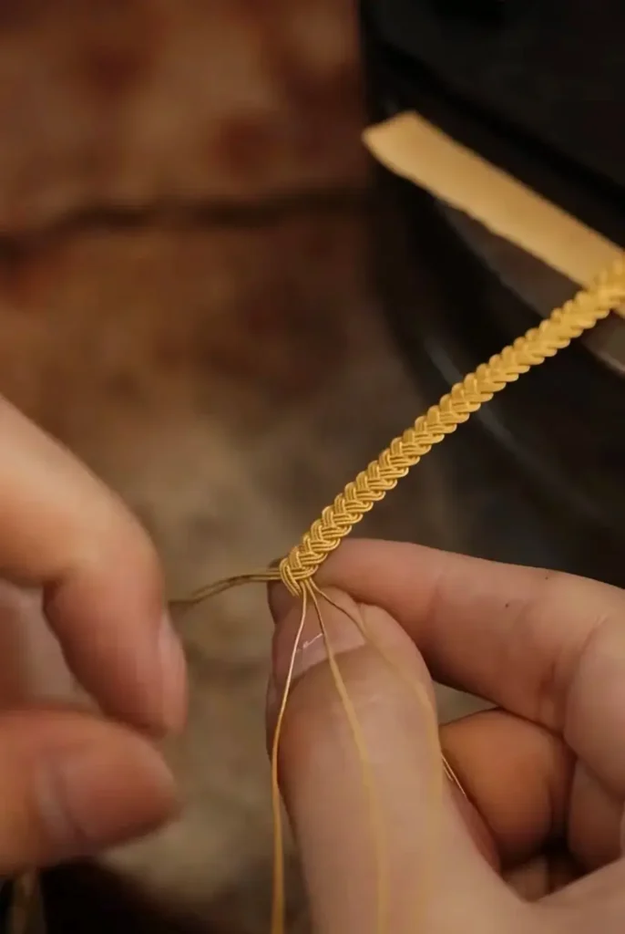An artisan braiding multiple fine metal strands into a decorative "Taozi" cord.
