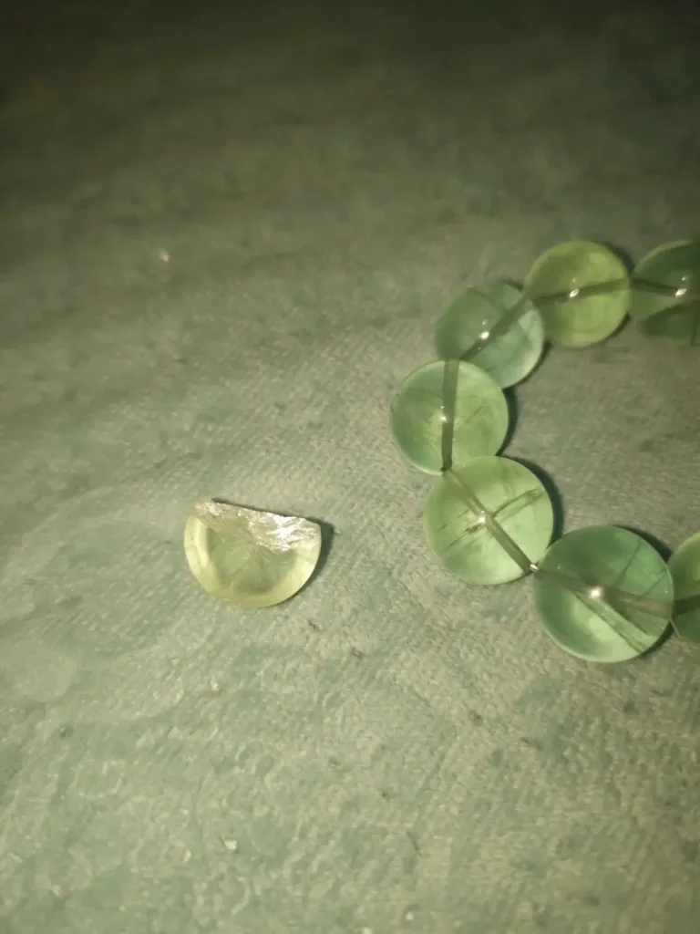 A shattered green fluorite bead showing a sharp internal fracture and a colorless crystal center.