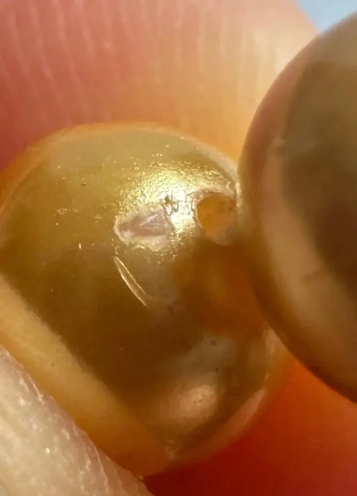 Macro view of a plastic imitation pearl showing surface mold lines and uniform pigment color.