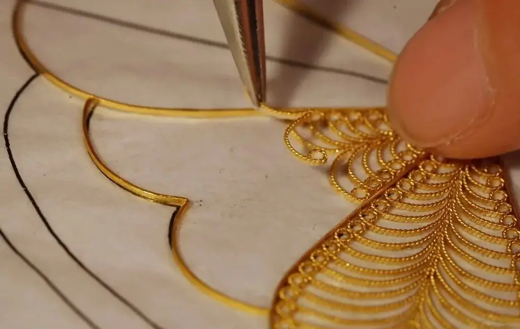 An artisan filling the interior of a pre-shaped gold filigree outline with decorative wires.