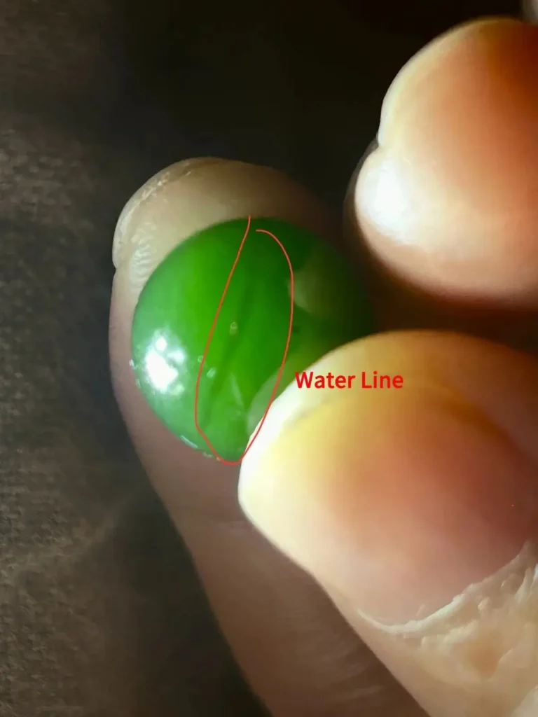 Green nephrite bead with red circle highlighting a linear water line.