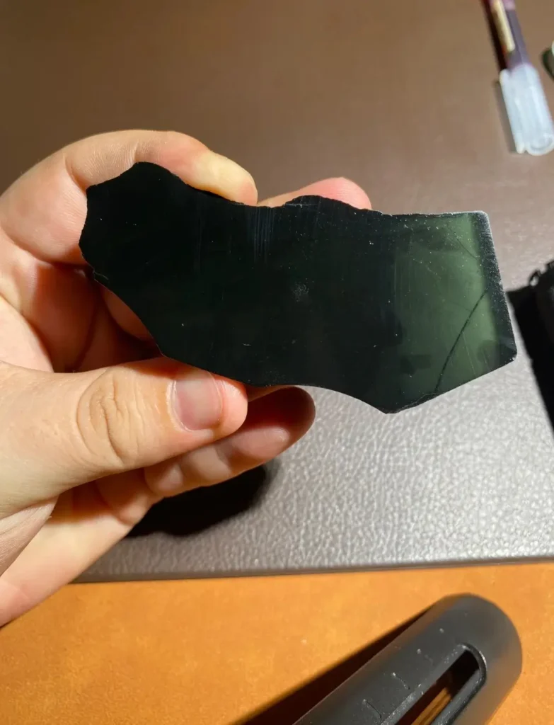 A hand holding a piece of Guangxi Black-Green jade showing an intense, jet-black appearance.