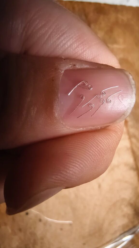 Macro view of 0.05mm silver wires resting on a human thumb for scale.