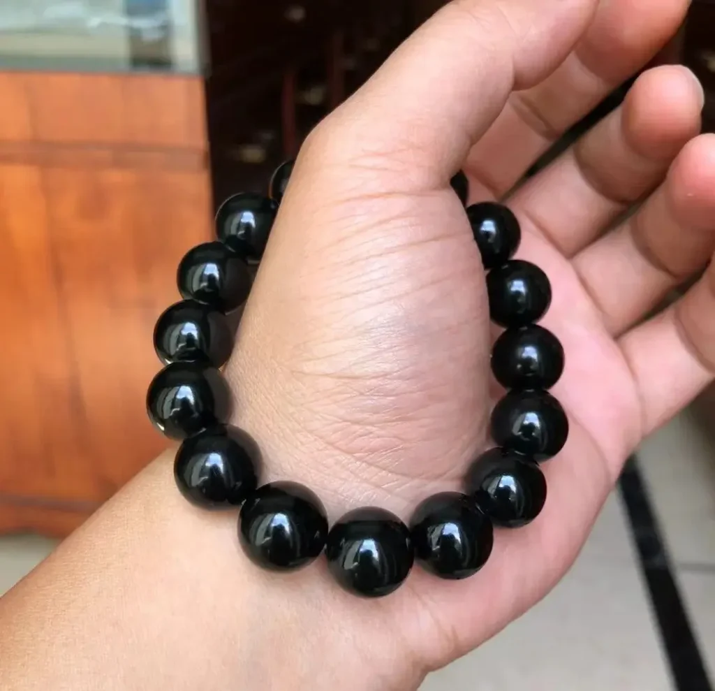 A hand holding a 14mm Xinjiang Hei Qing jade bead bracelet against a neutral background.