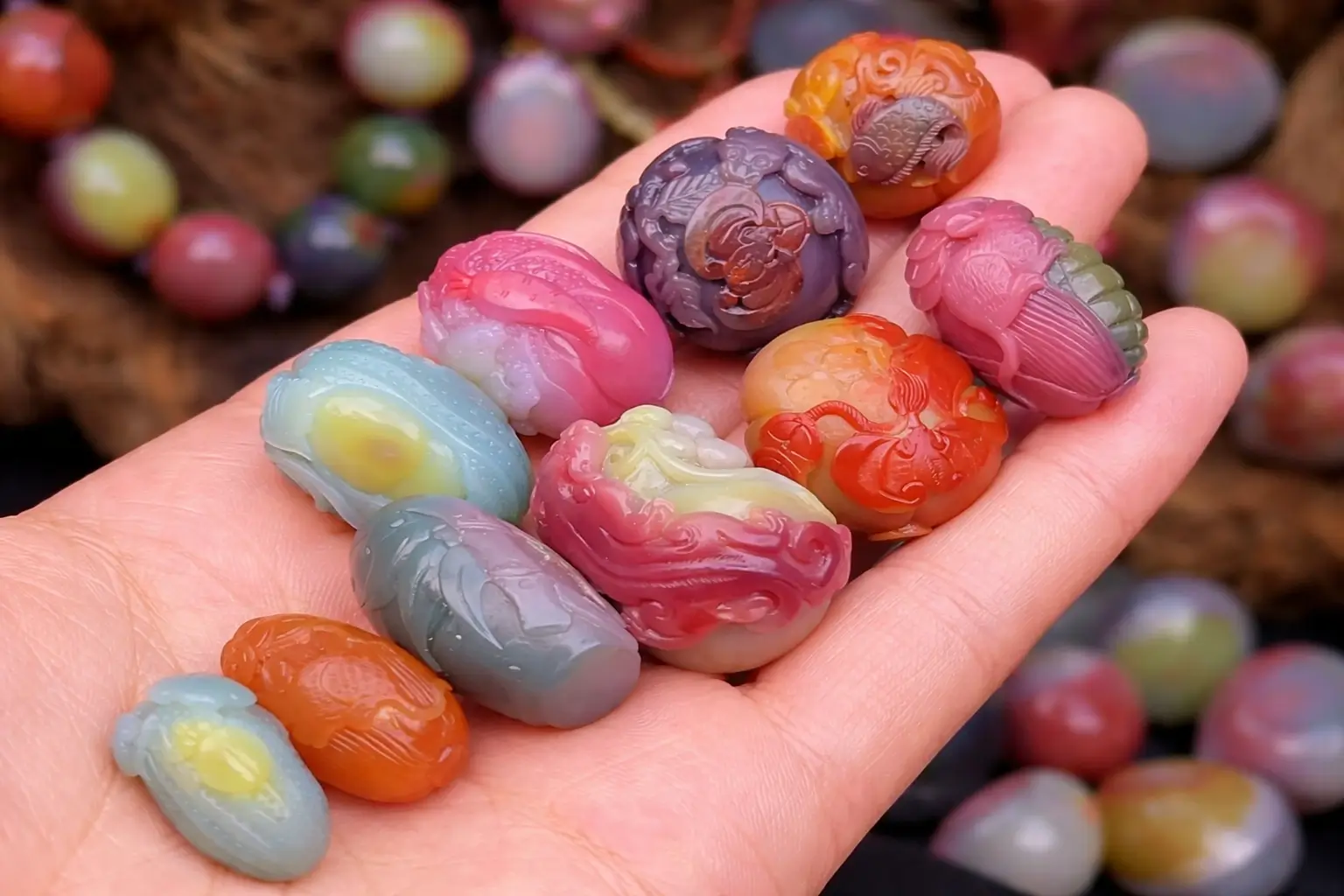 Handheld collection of small Yanyuan Agate carvings in pink, purple, green, and blue hues.